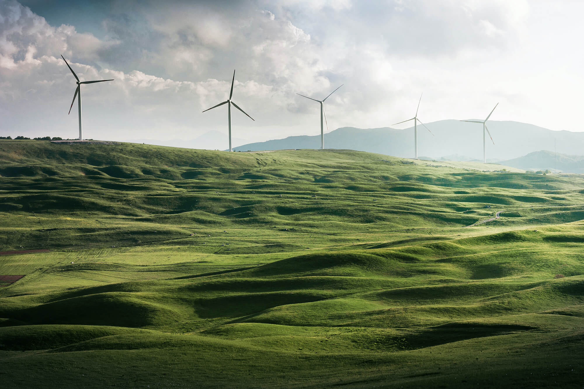 3 Windräder stehen in einer grünen Landschaft.
